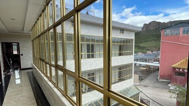 A corridor with large windows and a view of a building with multiple floors and a red structure in the background.