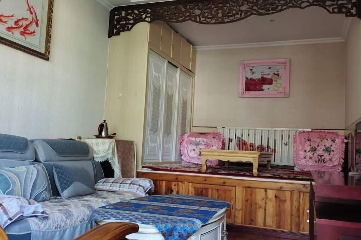 A room with a sofa, a bed, a wooden table, a radiator, and a decorative wall piece.