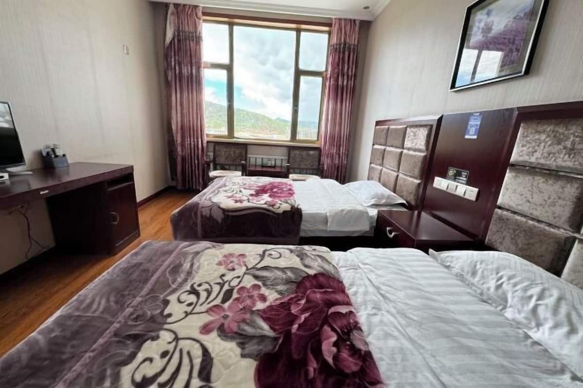 A hotel room with two beds, a desk, a chair, a window with curtains, and a mounted picture.
