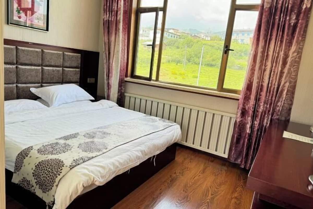A bedroom with a bed, a window with curtains, a radiator, and a wooden floor.