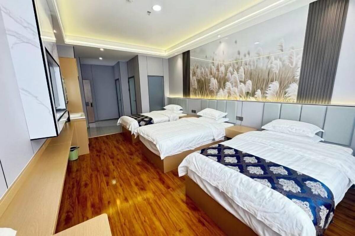 A hotel room with three beds, a wooden floor, a large wall mural, and a TV on the left wall.