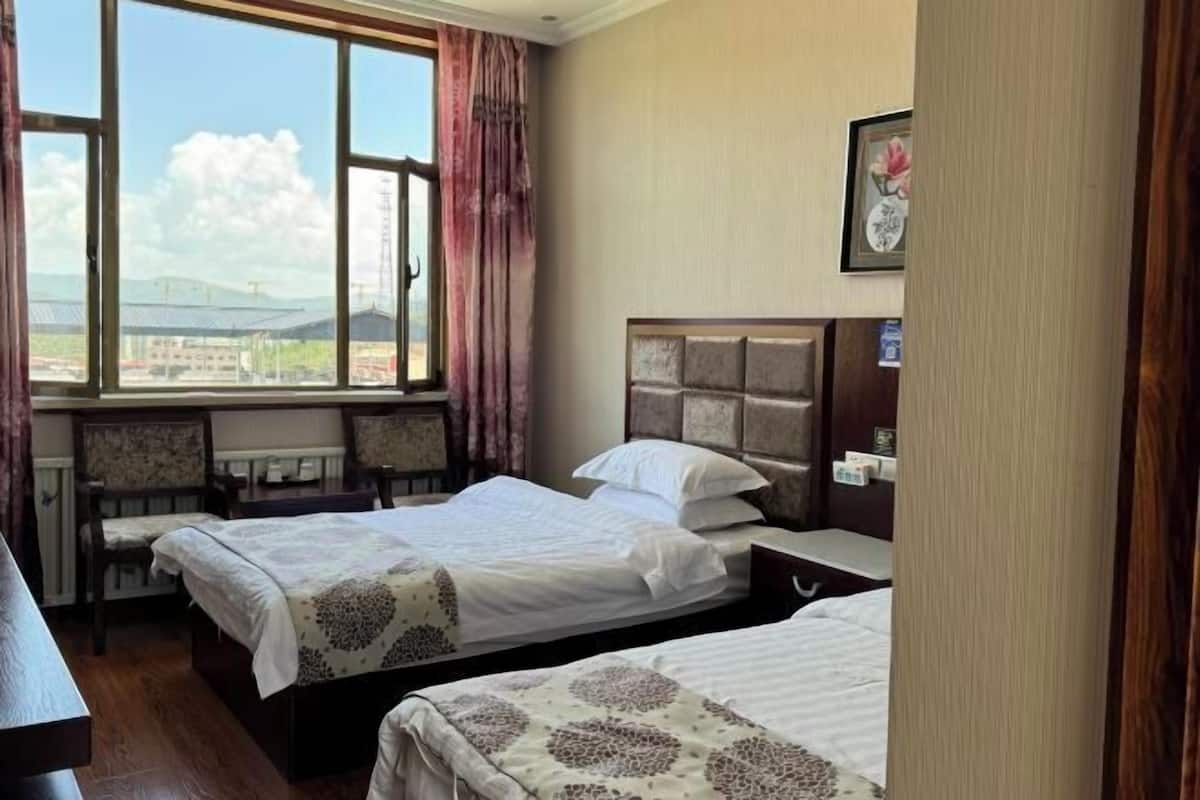 A hotel room with two beds, a window with a view of buildings, a desk, and a chair.