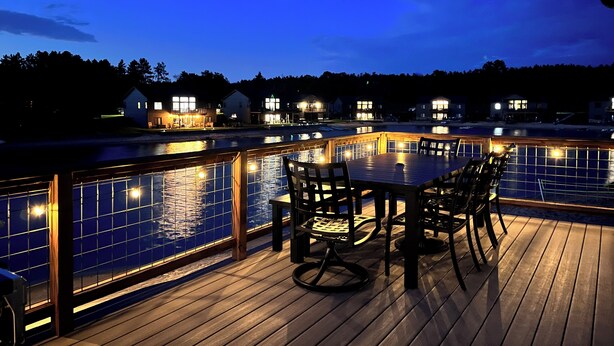 Una terraza de madera con piscina, rodeada de casas con ventanas iluminadas.