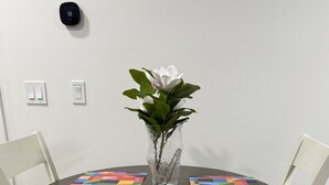 Ein runder Tisch mit einer Blumenvase, zwei Untersetzern mit geometrischem Muster und weißen Stühlen.
