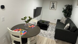 Ein modernes Wohnzimmer mit einem runden Esstisch, weißen Stühlen, einem schwarzen Sofa, einem schwarzen Couchtisch, einem Fernseher und einer Topfpflanze.