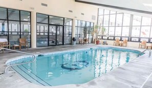 An indoor swimming pool with clear glass walls, a tiled floor, and several chairs and potted plants around the pool area. - Escape to Paradise in Avalon – Beautiful Condo Just Steps from the Beach (Avalon)