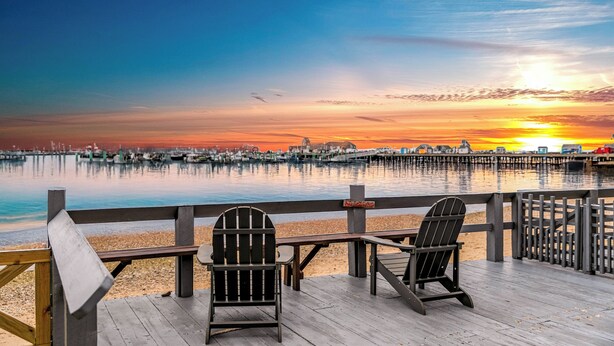 Una terraza de madera con dos sillas Adirondack que dan a un cuerpo de agua tranquilo durante el atardecer.