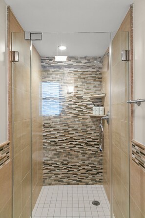 A glass-enclosed shower with a tiled mosaic wall, a small shelf with toiletries, and a ceiling light. - Pet-Friendly Beachside Condo + Parking on Comm St (Provincetown)