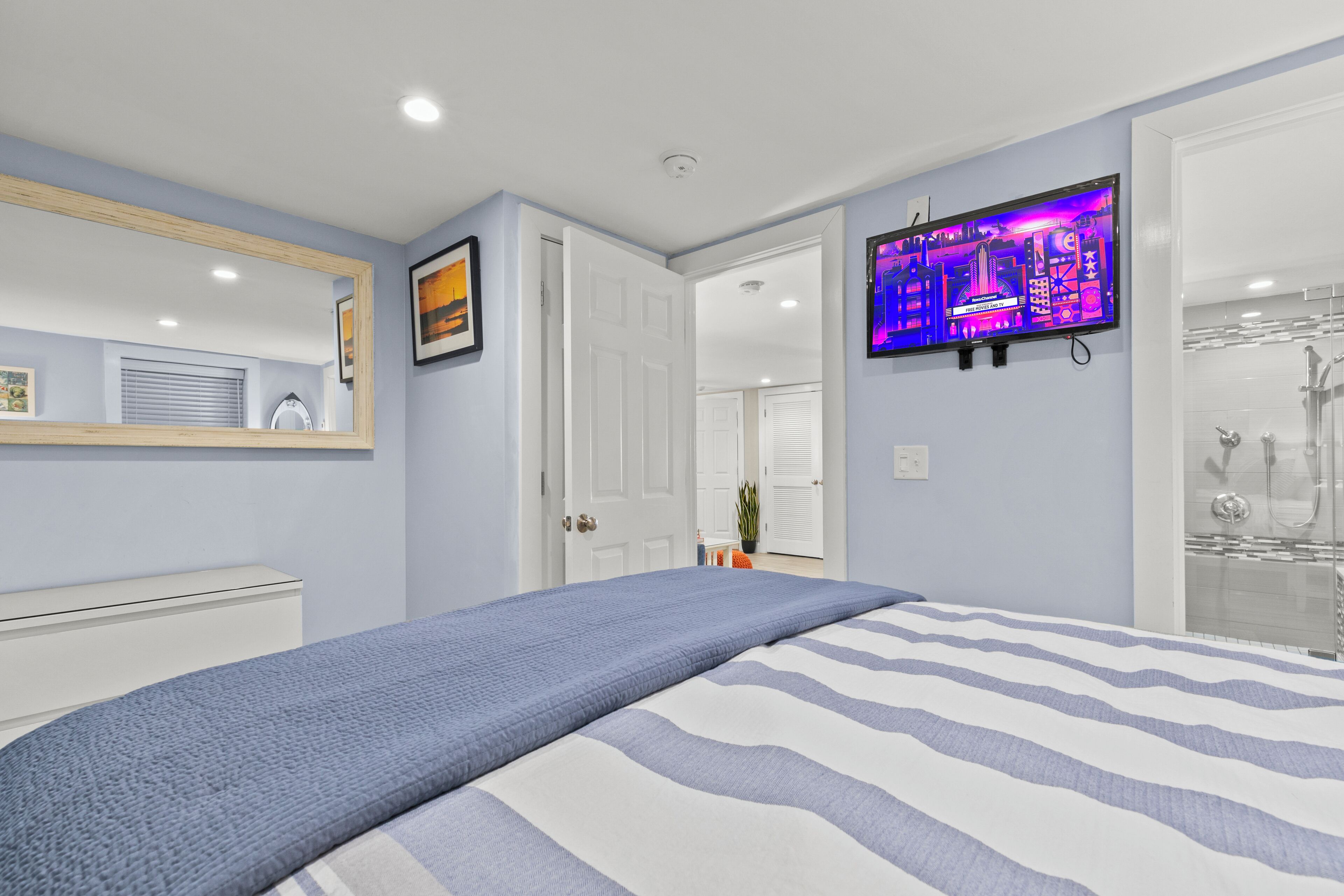 A bedroom with a bed, a TV mounted on the wall, and a bathroom with a glass shower.