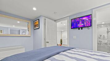 A bedroom with a bed, a TV mounted on the wall, and a bathroom with a glass shower.
