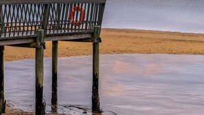 Un muelle de madera con un flotador, que conduce a una playa con aguas tranquilas y un cielo al atardecer.