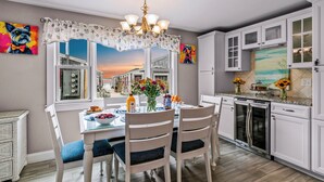 Una cocina moderna con armarios blancos, horno integrado y comedor con mesa para cuatro.