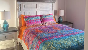 A bedroom with a wooden ceiling, a white headboard, a colorful bedspread, two bedside lamps, and a nightstand with a lamp. - Modern and brand new 3-bedroom condo with private rooftop pool  with majestic views. (Caye Caulker)