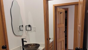 A bathroom with a wooden vanity, a large mirror, and a bowl sink. - Modern and brand new 3-bedroom condo with private rooftop pool  with majestic views. (Caye Caulker)