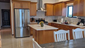 A modern kitchen with wooden cabinets, a stainless steel refrigerator, a central island with chairs, and a dining table. - Modern and brand new 3-bedroom condo with private rooftop pool  with majestic views. (Caye Caulker)