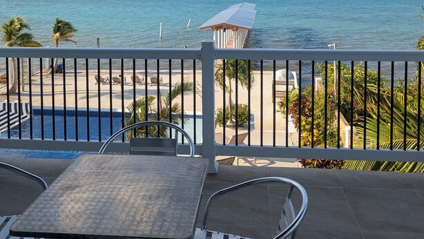 A balcony with a view of the ocean, a pool, and beach chairs. - Modern and brand new 3-bedroom condo with private rooftop pool  with majestic views. (Caye Caulker)