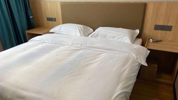 A hotel room with a bed, wooden headboard, two bedside tables, and a blue curtain. - Shuhao Hotel (Shanghai)