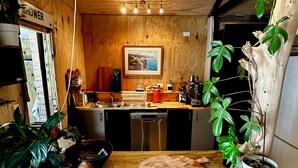 A kitchen with wooden cabinets, a sink, a coffee machine, and a potted plant. - Muriwai Surf Shack (Muriwai)
