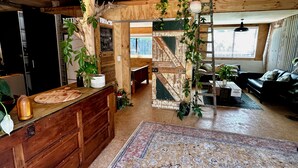 A rustic interior with wooden beams, a wooden counter with a chalkboard, and a staircase leading to an upper level. - Muriwai Surf Shack (Muriwai)