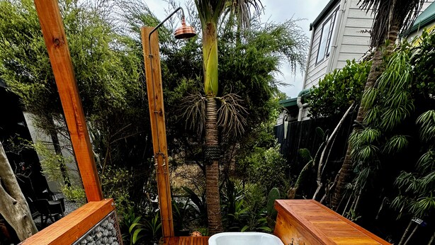 A wooden deck with a hot tub, surrounded by rocks and plants. - Muriwai Surf Shack (Muriwai)