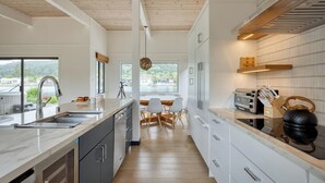 A modern kitchen with white cabinetry, a wooden ceiling, and a view of the outdoors. - Cozy 3BR by the lagoon w/ hot tub (Stinson Beach)
