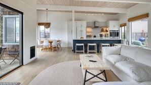 A modern kitchen with white cabinets, a central island, and a dining area with a round table and chairs. - Cozy 3BR by the lagoon w/ hot tub (Stinson Beach)
