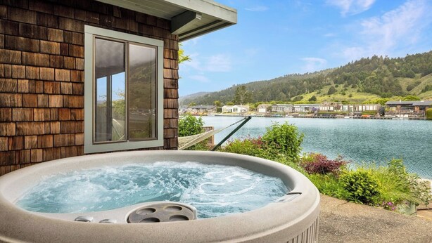 A hot tub on a balcony with a view of a lake and houses in the background. - Cozy 3BR by the lagoon w/ hot tub (Stinson Beach)
