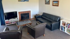 A living room with a fireplace, a television, a sofa, and two armchairs. - Forget your worries in our cosy farm cottage Spacious & relaxing with farm views (Ruawaro)