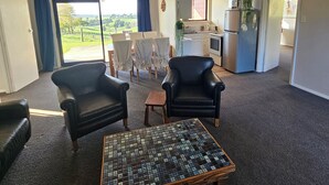 A living room with a sofa, armchairs, a coffee table, and a view of a green landscape through a sliding door. - Forget your worries in our cosy farm cottage Spacious & relaxing with farm views (Ruawaro)