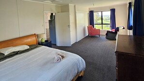 A hotel room with a bed, a desk, a chair, a wardrobe, and a window with curtains. - Forget your worries in our cosy farm cottage Spacious & relaxing with farm views (Ruawaro)