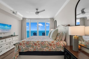 Une chambre avec un grand lit, un ventilateur de plafond, une télévision et une vue sur l’océan.