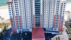 Un hotel de gran altura con varias plantas, fachada de vidrio central y un estacionamiento al frente.