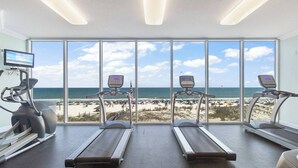 Un gimnasio con cintas de correr y una bicicleta estática, con vistas a la playa.