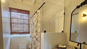 A bathroom with a toilet, shower curtain, sink, mirror, and a window with blinds.