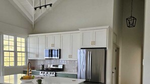 A spacious kitchen with white cabinets, a large island, stainless steel appliances, and pendant lighting.