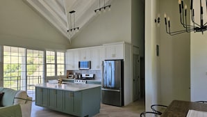 A spacious kitchen with white cabinets, a large island, stainless steel appliances, and a dining area with a wooden table.