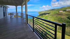 A covered balcony with a view of the sea and a hilly landscape.