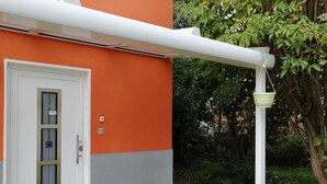 Un edificio con fachada naranja y gris, una puerta blanca con ventana y un toldo blanco.