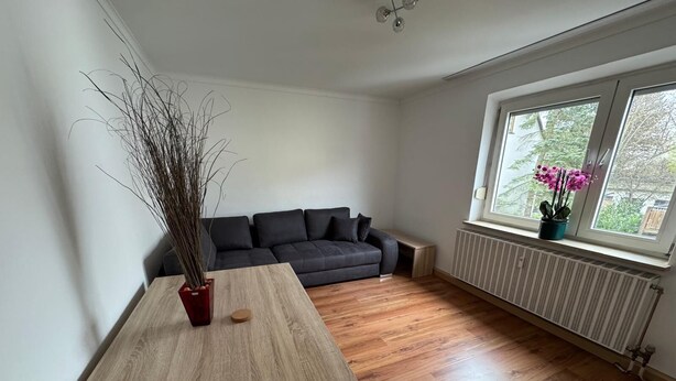 Una sala de estar moderna con una mesa de madera, un sofá negro y un ventanal con vistas a zonas verdes.