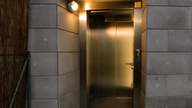 Un étroit puits d’ascenseur aux parois métalliques, avec un luminaire au-dessus.