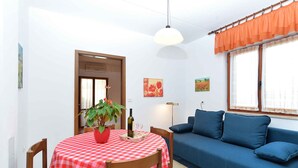 A room with a dining table covered with a checkered tablecloth, a blue sofa, a potted plant, and a painting on the wall.