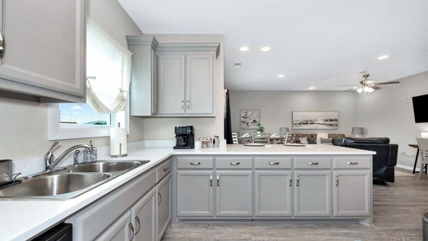 A modern kitchen with grey cabinetry, a large island, and a dining area with a black couch.
