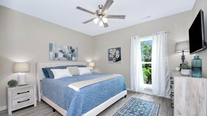 A bedroom with a bed, a ceiling fan, a nightstand, a TV, and a window with curtains.