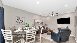 A modern living room with a dining area, a ceiling fan, and a flat-screen TV mounted on the wall.