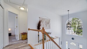 A staircase with white railings, a world map on the wall, and a view of greenery through a window.
