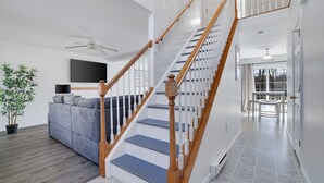 A modern living room with a grey sofa, wooden staircase, and a ceiling fan.