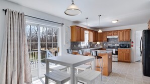 A modern kitchen with wooden cabinets, a central island, and a dining area with white furniture.