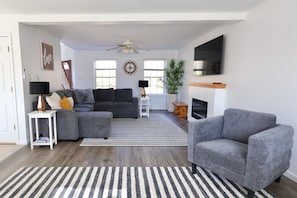 A living room with a grey sofa, a striped rug, a ceiling fan, and a TV mounted on the wall.
