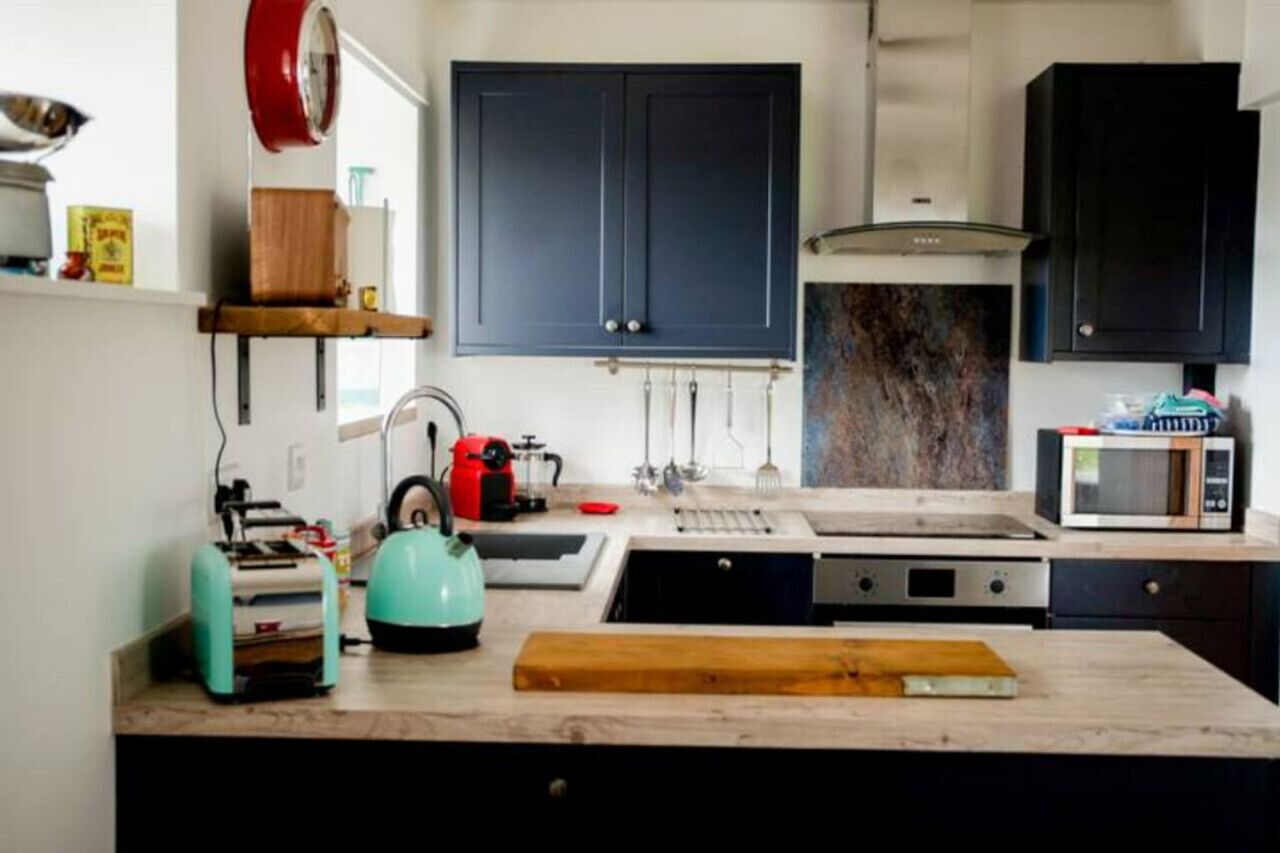 A modern kitchen with dark cabinets, a sink, a stove, a microwave, and a kettle.