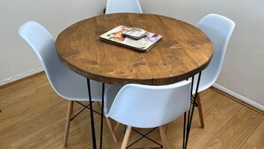 Een ronde houten tafel met een tijdschrift erop, omringd door vier witte stoelen met zwarte metalen poten.